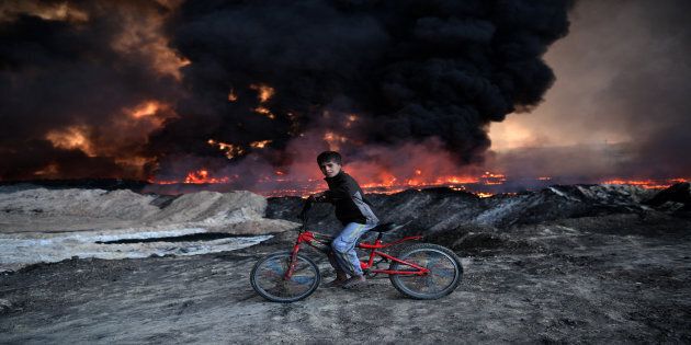 A boy pauses on his bike as he passes an oil field set alight by retreating ISIS fighters ahead of the Mosul offensive, on October 21, 2016 in Qayyarah, Iraq.