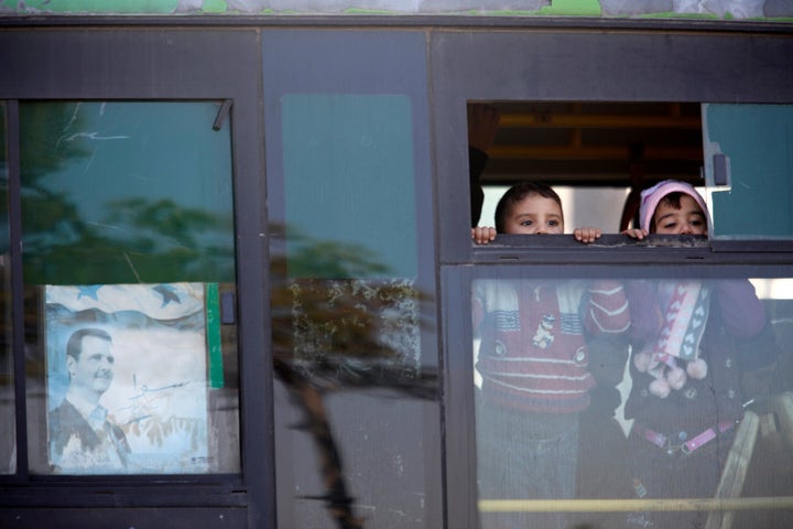 Children who came back with their families to inspect their homes, ride a bus in goverment controlled Hanono housing district in Aleppo, Syria December 4, 2016. The poster shows Syria's president Bashar al-Assad and reads in Arabic "Together".