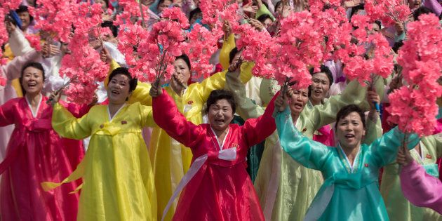 Women wearing traditional Korean dress wave flowers and shout slogans during a mass rally marking the 105th anniversary of the birth of late North Korean leader Kim Il-Sung.