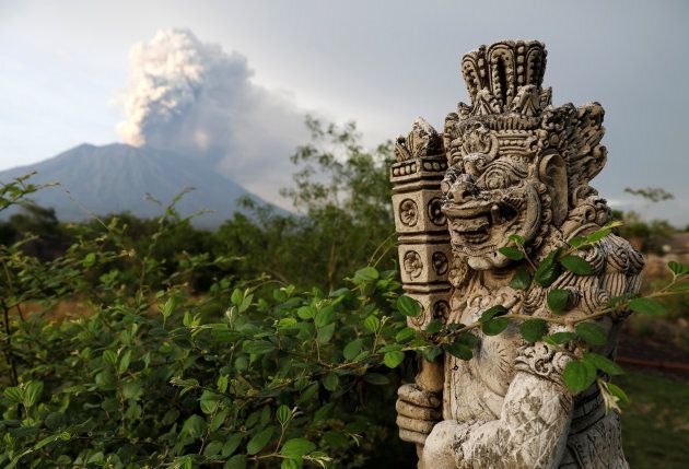 A statue on a bridge is seen as Mount Agung volcano erupts in the background near Kubu, Karangasem Regency, Bali.