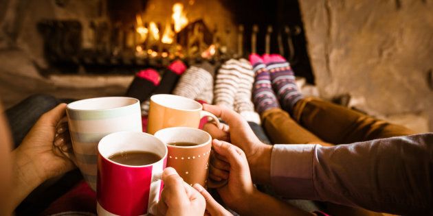 Four people warming their feet by the fireplace and drinking hot chocolate.