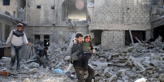 A man carries an injured boy as he walks on rubble of damaged buildings in the rebel held besieged town of Hamouriyeh, eastern Ghouta, near Damascus, Syria, February 21, 2018.