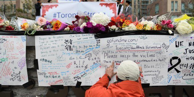 A man writes a message at a memorial on Yonge Street the day after a suspect drove a rented van down sidewalks, striking pedestrians in Toronto.