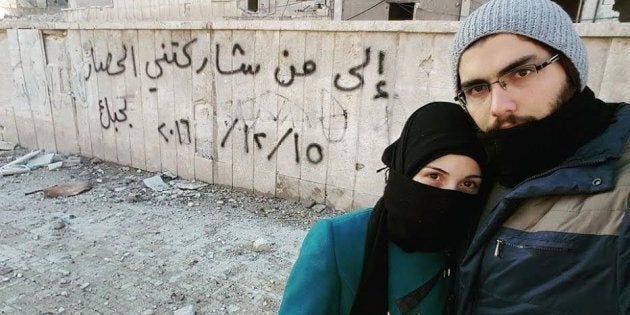 Marwa and Salih pose in front of a graffiti message they left in Aleppo.