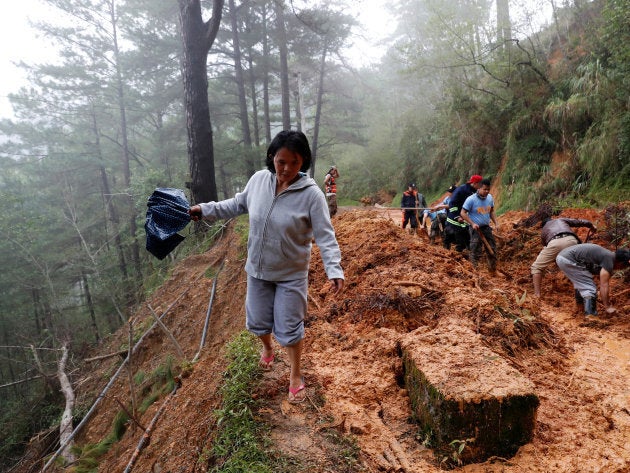 A resident walks on the side of a road as police officers and fire marshals clear debris and fallen trees caused by a landslide at the height of Typhoon Mangkhut.