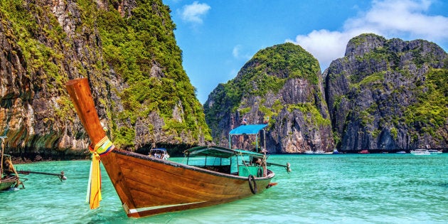 Long tail wooden boat at Maya Bay on Ko Phi Phi Le, made famous by the movie titled 'The Beach'. Beautiful cloudscape over the turquoise water and green rocks in Maya Bay, Phi Phi Islands, Thailand.