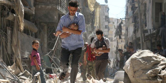 Syrian men carrying babies make their way through the rubble of destroyed buildings.