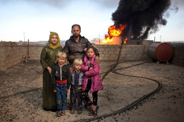 Ibrahim Mohammed with wife Soma Selwan stand on the roof of their home with their children Luma 11, Aws 6, and Mutasm 5. They live next to a burning oil well in Qayarrah. Soma says she is always cleaning and it just keeps coming.