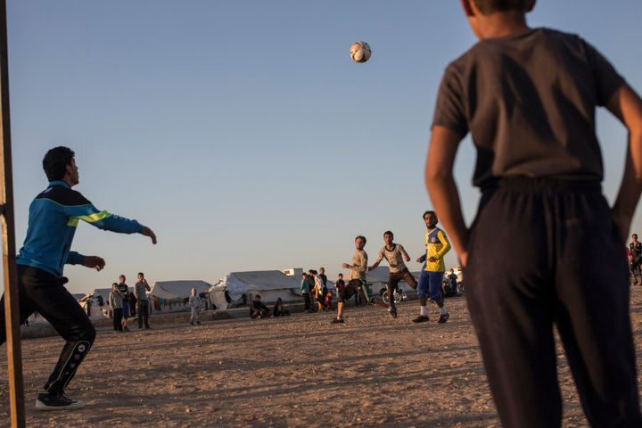 Residents of Hassan Sham camp for people displaced by the war with ISIS play football on a rocky pitch next to on the camp's main thoroughfare, near the town of Khazer, Iraq.