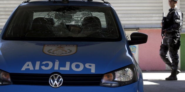 A policeman walks past a police car damaged during a protest at the Mangueira slum in Rio de Janeiro, Brazil August 11, 2015. In the city of Campinas on New Year's Eve, a gunman shot and killed at least 11 people.