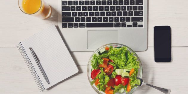 Healthy business lunch in the office, top view of vegetable salad on white wooden desk near laptop computer keyboard. Salad bowl, juice, mobile phone and notepad with pen flat lay. Snack at break time