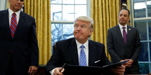U.S. President Donald Trump, flanked by Vice President Mike Pence (L) and White House Chief of Staff Reince Priebus (R), looks up while signing an executive order on the reinstatement of the Mexico City Policy in the Oval Office of the White House in Washington January 23, 2017. REUTERS/Kevin Lamarque