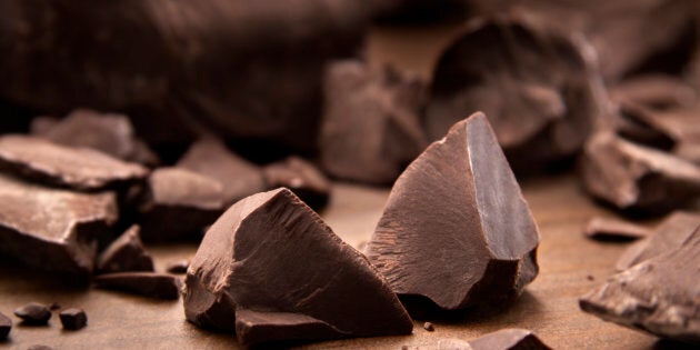 Pieces of dark chocolate spread out on a wooden background.