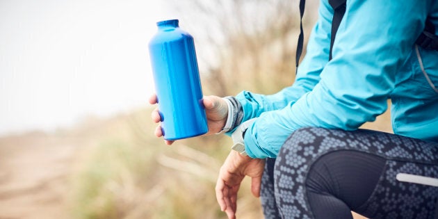 Midsection of traveler holding water bottle. Female is wearing casuals. She is sitting on rock.