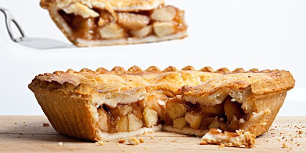 A whole apple pie with a slice removed and held overhead on a white background.
