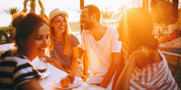 Smiling friends spending some quality time during the dinner party, outside on a beach, talking and laughing