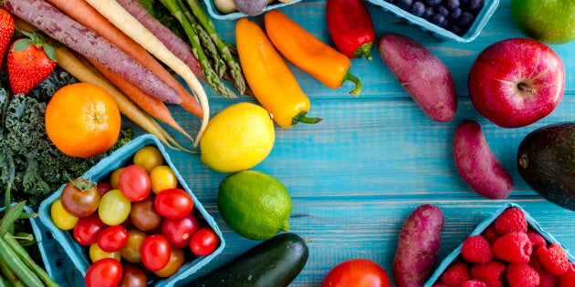 Variety of fresh raw organic fruits and vegetables in light blue containers sitting on bright blue wooden background