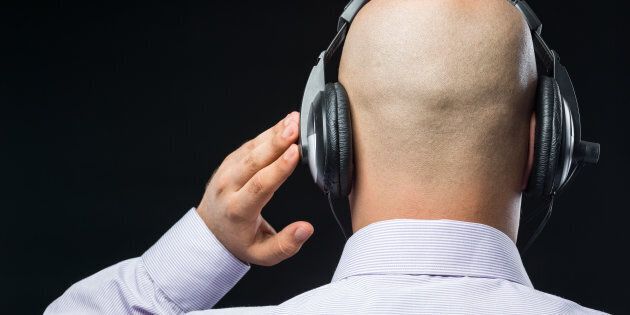 Bald man with headphones listening in dark on black background.