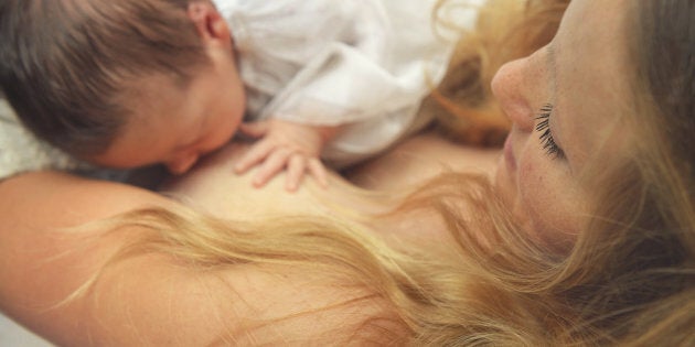 Beautiful mother breastfeeding her newborn who is holding her breast and sucking milk.