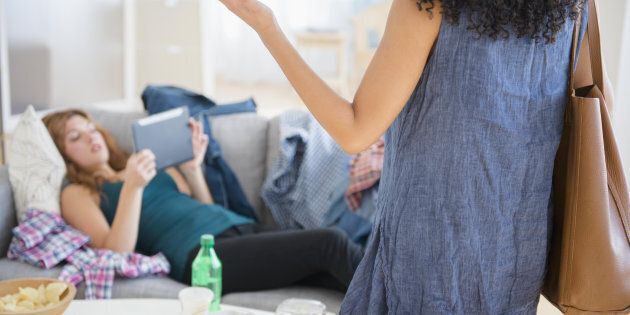 Woman frustrated at lazy roommate using digital tablet on sofa