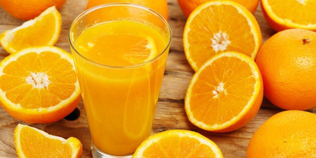 glass of orange juice with oranges on wooden surface