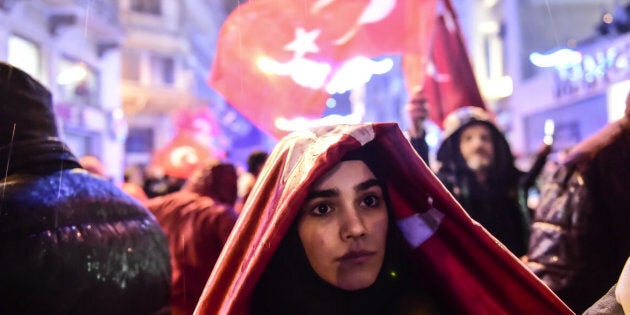 A woman covers herself from rain with the Turkish national flag during a demonstration on March 12, 2017 in front of the Netherlands consulate in Istanbul. The Dutch embassy in Ankara and consulate in Istanbul have been sealed off for 'security reasons', Turkish foreign ministry sources said on Saturday, as tensions soar between Turkey and the Netherlands. / AFP PHOTO / YASIN AKGUL (Photo credit should read YASIN AKGUL/AFP/Getty Images)