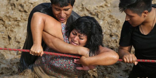 Two men help a woman cross a flooded street after a river overflowed, sending torrents of mud and water rushing through the streets in Huachipa last Friday.