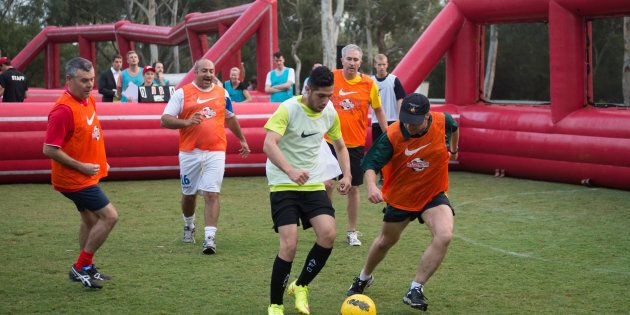 Minister for Health and Sport, Greg Hunt, (centre, in hat) plays against the Street Socceroos team at the Big Issue competition at parliament on Wednesday.