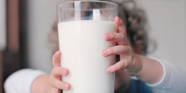 Boy (2-4) holding glass of milk on table, close-up