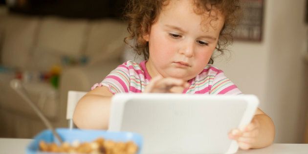 cute little girl eating cornflakes and playing on digital tablet