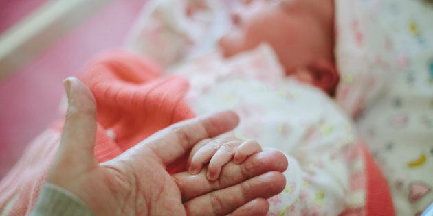 Stock image of a newborn baby holding on to mother's hand while in hospital a few hours after being born.