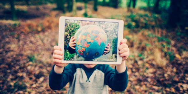 Child outdoors in the woods holding up an electronic tablet with an image of a globe on it.