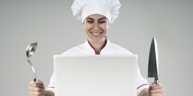 happy woman chef looking at the laptop computer with knife and ladle in her hands