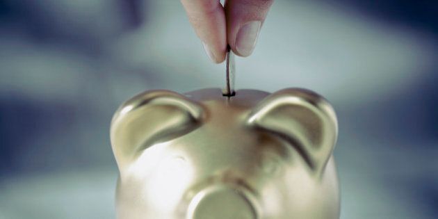 Person's hand putting coin into a piggy bank