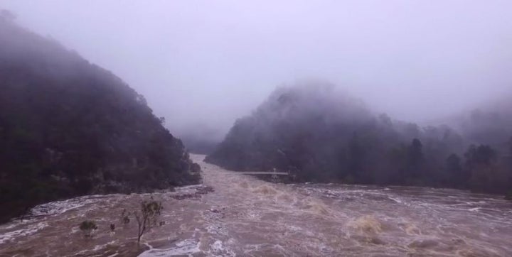 A spindly footbridge appears small and fragile compared to the floodwaters.