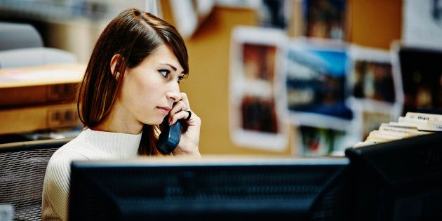 Businesswoman sitting at workstation in office on phone with client