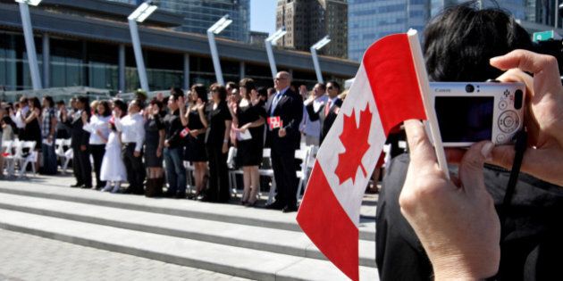 A woman takes a photograph while holding a Canadian flag as a group of 61 new Canadians take the oath of citizenship during a citizenship ceremony held as part of Canada Day celebrations in Vancouver, B.C., on Wednesday July 1, 2009. THE CANADIAN PRESS/Darryl Dyck