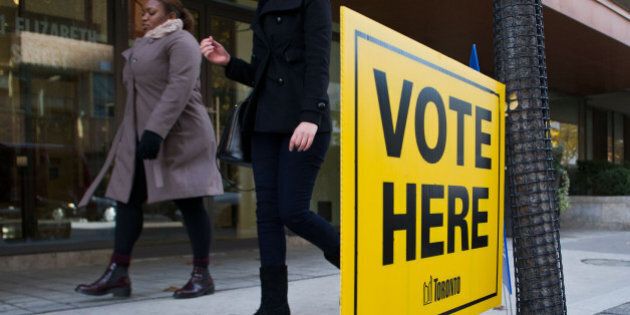 Women walk past a 'Vote Here' sign displayed outside of One City Hall in Toronto, Ontario, Canada, on Monday, Oct. 27, 2014. Toronto votes for a mayor today in an election that pits Doug Ford's subways against John Tory's surface rail in a race that has largely revolved around easing one of North America's longest commute times. Photographer: Galit Rodan/Bloomberg via Getty Images