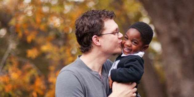 Father kissing his adopted toddler son who is African-American at Old Settler's Park in Round Rock, Texas.