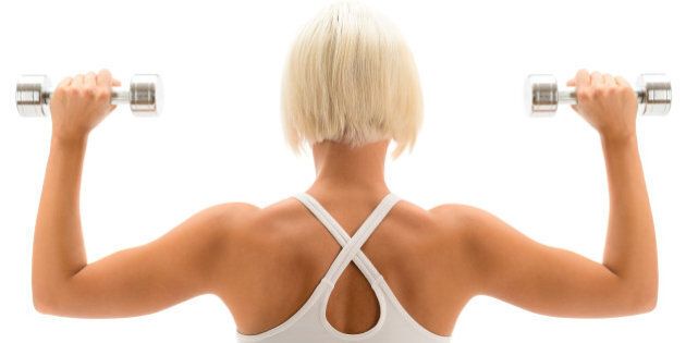 Back view portrait muscular blond woman holding dumbbell on white