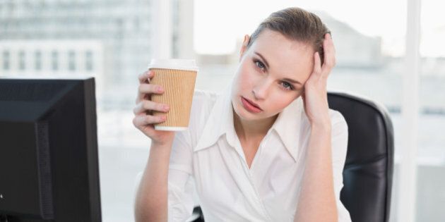 Stressed businesswoman holding disposable cup looking at camera in her office