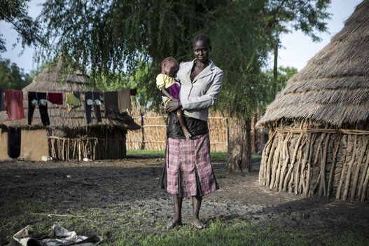 Alia holds her daughter Nyadoth outside their temporary home in Akobo, South Sudan