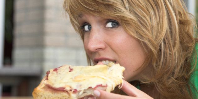 Pretty blond girl taking a bite out of her toasted sandwich