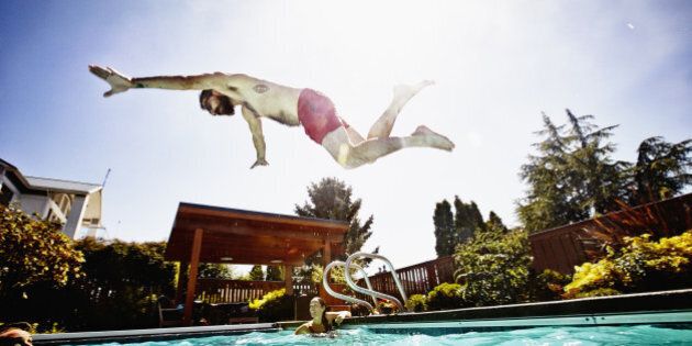 Man in mid air diving towards friends swimming in outdoor pool during pool party