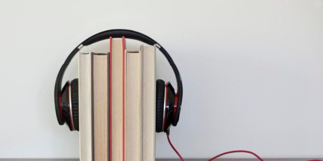Headphones around a group of books to suggest the concept of listening to audios books.