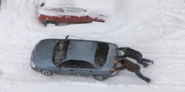 People push a car under snowfall in Kiev, Ukraine, Saturday, March 23, 2013. Heavy snow storms from the Balkan region have been stricken Ukraine since Friday. (AP Photo/Efrem Lukatsky)