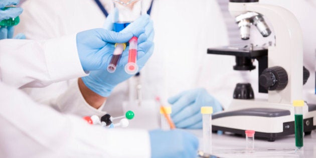 Unrecognizable group of scientists working inside a research laboratory. Scientists hold test tubes, chemicals. One writes notes on a chart. Microscope. They are conducting genetic science experiments.