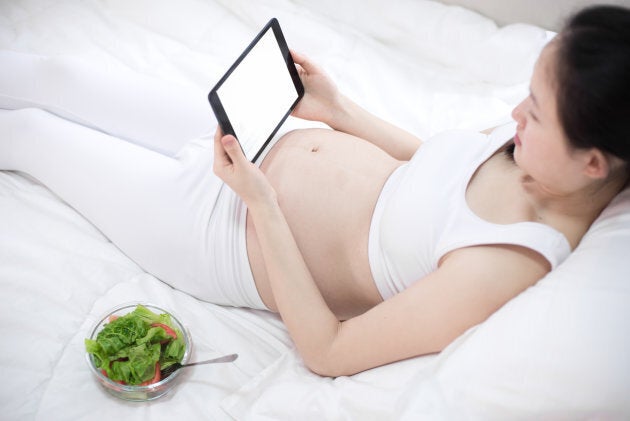 pregnancy, technology, people and expectation concept - close up of pregnant woman with tablet pc computer in bed at home