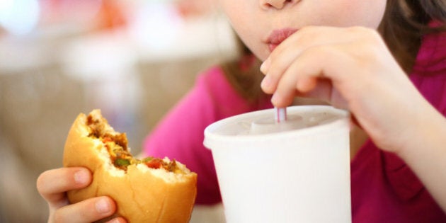 Closeup of little girl eating burger and drinking soda. Cut for unrecognition.The girl is elementary age and wearing pink t-shirt