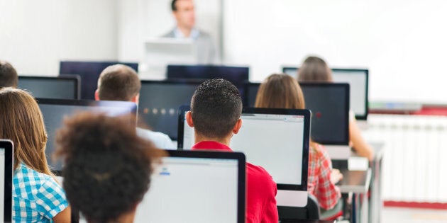 Rear view of lager group of people at a computer class. Teacher is teaching in the background.